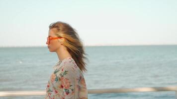 une femme dans des lunettes de soleil et une floral chemise des stands par le océan video