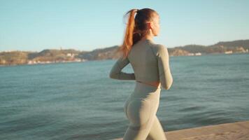 Young adult fitness woman jogging by embankment area coastal city in beautiful sunny day. video