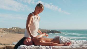 Woman enjoying professional spa hand massage lying on special table on beach during vacation. Massage therapist giving relaxing massage client's arms and shoulders video