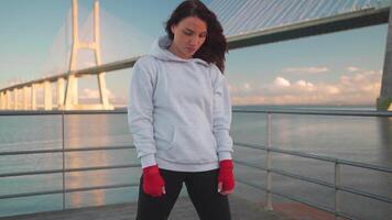 Woman shadow taking fighting pose with her hands wrapped in red boxing tapes with city seascape background. video