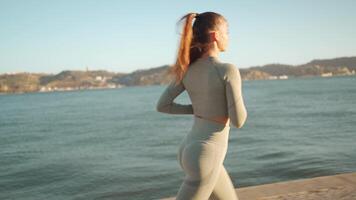 Young adult fitness woman jogging by embankment area coastal city in beautiful sunny day. video