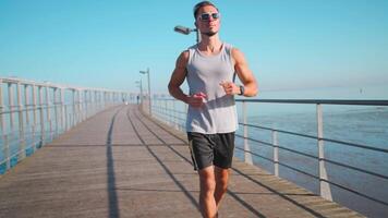 mannetje jogger rennen Aan brug zonnig dag. atleet aan het doen cardio opleiding. video