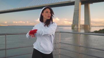 mulher sombra levando brigando pose com dela mãos embrulhado dentro vermelho boxe fitas com cidade marinha fundo. video