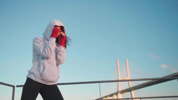 Woman shadow boxing with her hands wrapped in red boxing tapes in park with punching box. video