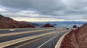 Scenic Route Overlooking Lake Mead, A highway winds through the desert with a panoramic view of Lake Mead in the distance under a cloudy sky. video