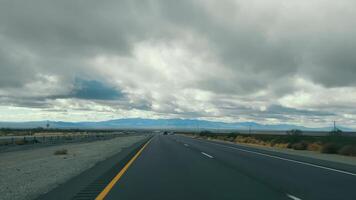 Highway to the Mountains under Overcast Skies, A straight highway leads towards a dramatic mountain range under stormy skies. video