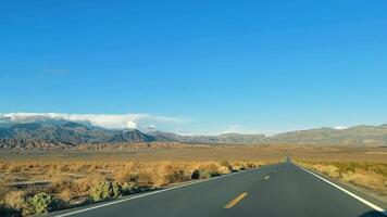 Desert Road Leading to Mountain Range, An open highway meanders toward a stunning mountain range under a clear blue sky. video