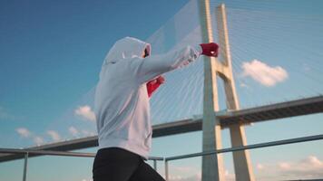 Woman shadow boxing with her hands wrapped in red boxing tapes in park with punching box. video