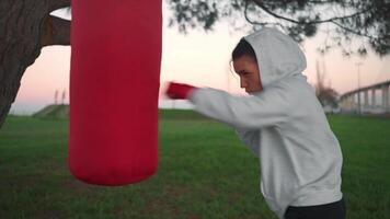 a young girl in a hoodie is hitting a punching bag video
