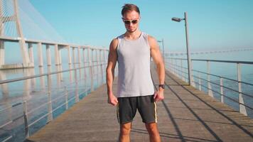 mannetje jogger rennen Aan brug zonnig dag. atleet aan het doen cardio opleiding. video