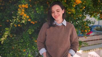 a woman in a sweater and jeans standing next to an orange tree video