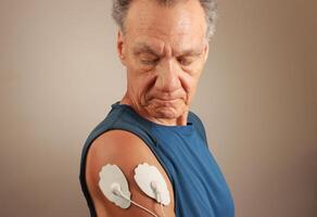 Man using an Electro Therapy Massager or Tens Unit on his Deltoids for pain relief for Muscles and Joints photo