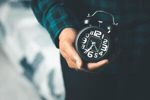 Time management concept. Man hands holding Black retro alarm clock. Time to wake up for the morning routine photo