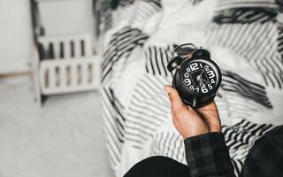 Time management concept. Man hands holding Black retro alarm clock. Time to wake up for the morning routine photo