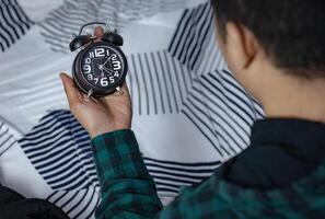 hora administración concepto. asiático hombre mirando a negro retro alarma reloj. hora a despertar arriba para el Mañana rutina foto