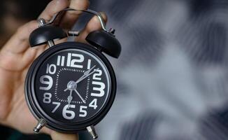 Time management concept. Man hands holding Black retro alarm clock. Time to wake up for the morning routine photo