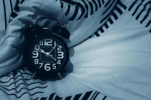 Bedtime and rest concept. Close up of Black alarm clock on bed showing 10 o'clock pm. Time to sleep photo