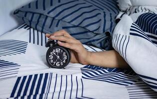 fecha límite y hora administración concepto. hombre manos participación negro alarma reloj en cama. hora a despertar arriba para el Mañana rutina foto