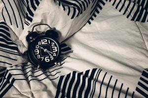 Bedtime and rest concept. Close up of Black alarm clock on bed showing 10 o'clock pm. Time to sleep photo