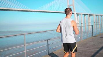 masculino corredor corrida em ponte ensolarado dia. atleta fazendo cardio treinamento. video