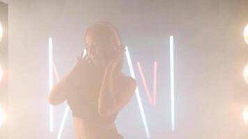 artístico joven mujer auriculares disfrutar música bailando en retroiluminado niebla fumar adentro. video