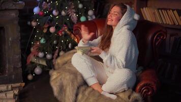 mujer leyendo libro sentado acogedor cuero Sillón con Navidad árbol en antecedentes. video