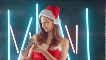 vrouw gekleed in de kerstman kostuum de kerstman hoed gooit geld terwijl staand verlichte neon achtergrond. video