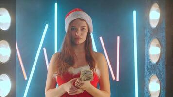 Woman dressed in Santa costume Santa hat throws money while standing illuminated neon background. video