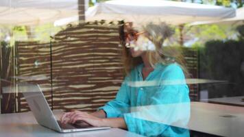 ein Frau im Brille Sitzung beim ein Tabelle mit ein Laptop. Fernbedienung Arbeiten Konzept video