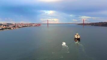 Aerial drone shot of cargo ship and small boat moving in sea along mountains under cloudy sky. video