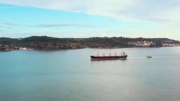 Aerial drone shot of cargo ship and small boat moving in sea along mountains under cloudy sky. video