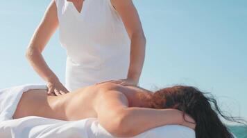 Woman enjoying professional spa hand massage lying on special table on beach during vacation. Massage therapist giving relaxing massage client's arms and shoulders video