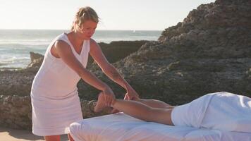 vrouw genieten van professioneel spa hand- massage aan het liegen Aan speciaal tafel Aan strand gedurende vakantie. massage therapeut geven ontspannende massage van de klant armen en schouders video