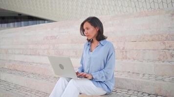 Businesswoman sitting on stairs using laptop in park. video