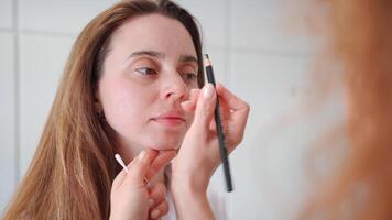 Master applies white markings to correct shape of eyebrows with a special pencil. video