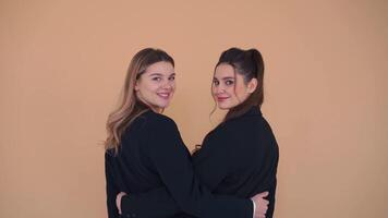 Medium portrait shoot of two young business woman dressed black jacket standing studio over pastel color background. She is shy laughs talk and speak. Female modern business person video