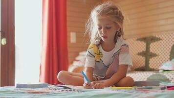 un pequeño niña sentado en un cama con un marcador y un lápiz video