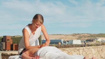 vrouw genieten van professioneel spa hand- massage aan het liegen Aan speciaal tafel Aan strand gedurende vakantie. massage therapeut geven ontspannende massage van de klant armen en schouders video