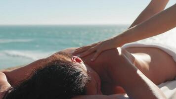 vrouw genieten van professioneel spa hand- massage aan het liegen Aan speciaal tafel Aan strand gedurende vakantie. massage therapeut geven ontspannende massage van de klant armen en schouders video