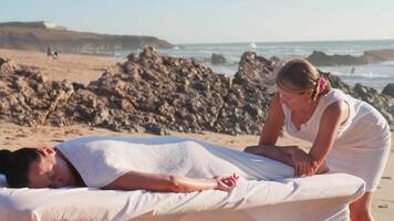 Woman enjoying professional spa hand massage lying on special table on beach during vacation. Massage therapist giving relaxing massage client's arms and shoulders video