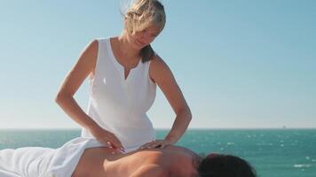 kvinna njuter professionell spa hand massage liggande på särskild tabell på strand under semester. massage terapeut ger avkopplande massage klientens vapen och axlar video
