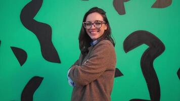 a woman in glasses standing in front of a green wall video