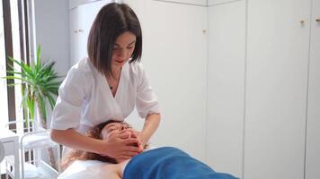 masaje terapeuta masajear cabeza, espalda y cuello a mujer en cosmetología clínica. cosmetólogo haciendo protección de la piel y estímulo procedimiento. spa tratamiento y masaje en belleza salón parte superior ver video
