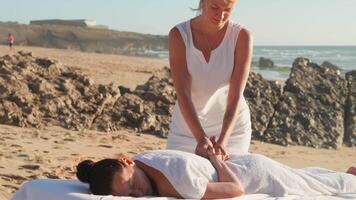 mulher desfrutando profissional spa mão massagem deitado em especial mesa em de praia durante período de férias. massagem terapeuta dando relaxante massagem do cliente braços e ombros video