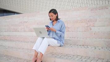 femme d'affaires utilisation portable Extérieur séance escaliers Contexte. caucasien femelle affaires la personne 30 ans dactylographie portable clavier. éloigné travail pigiste concept. free-lance emploi ses Nouveau Ordinaire video