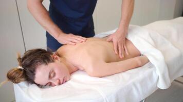 manlig massager ger terapeutisk och avkopplande, djup vävnad stimulerande tillbaka massage till en caucasian kvinna patient video