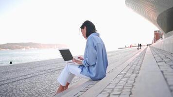 mujer de negocios utilizar ordenador portátil al aire libre sentado escalera antecedentes. caucásico hembra negocio persona 30 años mecanografía ordenador portátil teclado. remoto trabajo persona de libre dedicación concepto. Lanza libre trabajo sus nuevo normal video