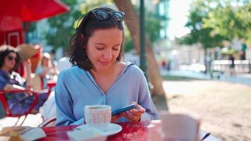 mooi vrouw zittend buitenshuis cafetaria gebruik smartphone chatten met vrienden. mooi Kaukasisch bedrijf vrouw koffie pauze. voorkant visie portret schieten. meisje met zonnebril Aan hoofd resting cafe video