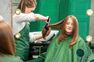 peluquero haciendo cortes de cabello para el mujer mientras peinada con cepillo para el pelo, peine en un pelo salón. foto