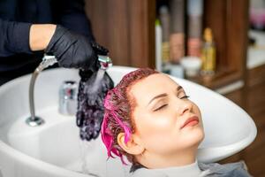 Lavado teñido hembra cabello. profesional peluquero lavados rosado color pintar apagado de un cliente. joven caucásico mujer teniendo su pelo lavado en un belleza salón. foto